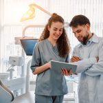 Two dentist doctors are standing in a dental office and looking at a tablet. Medicine, dentistry.